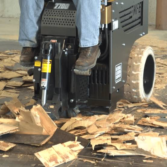 Close-up of a ride-on floor scraper lifting flooring material.
